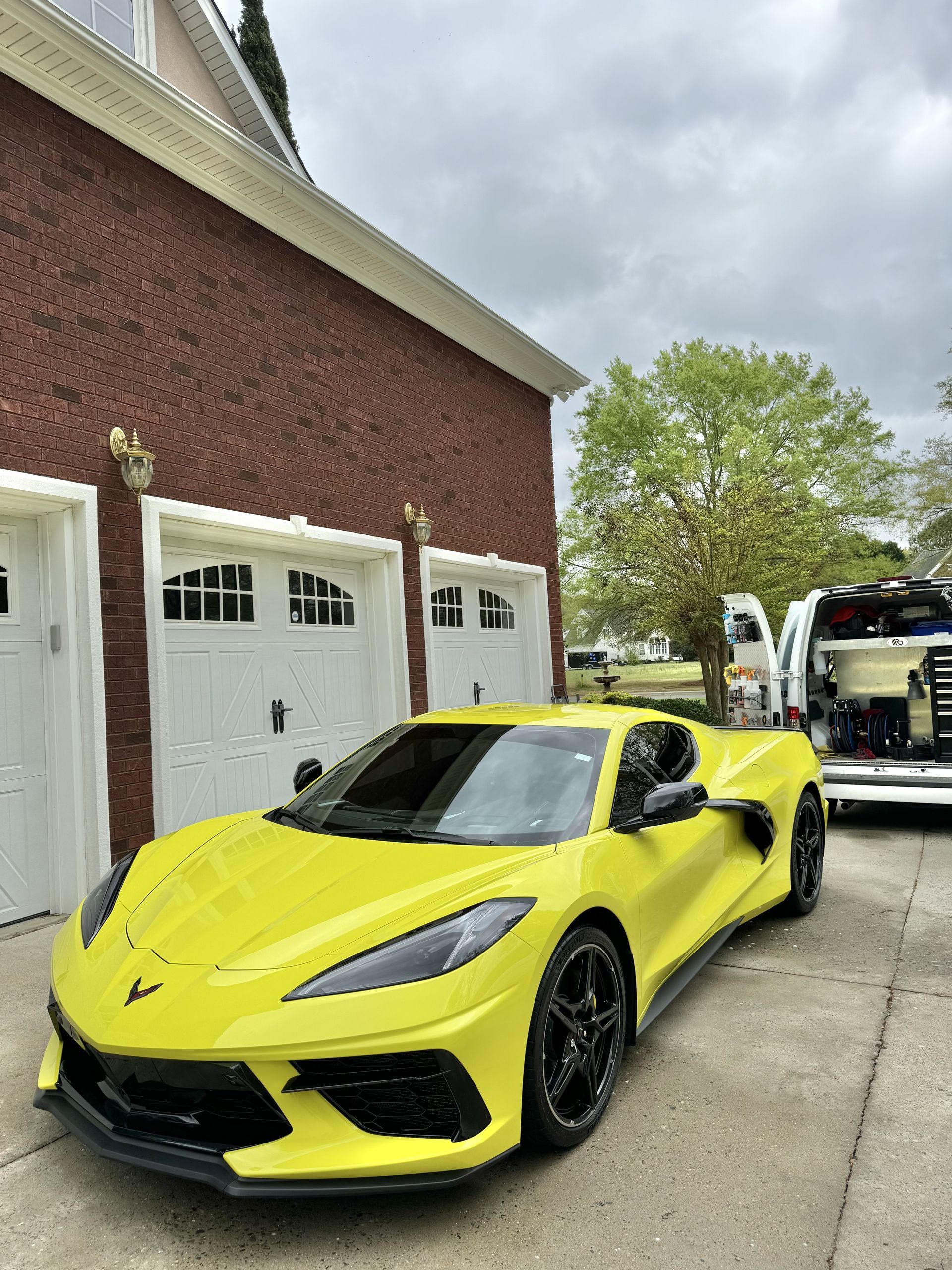 Yellow Corvette parked in front of a brick building with white garage doors; cloudy sky.