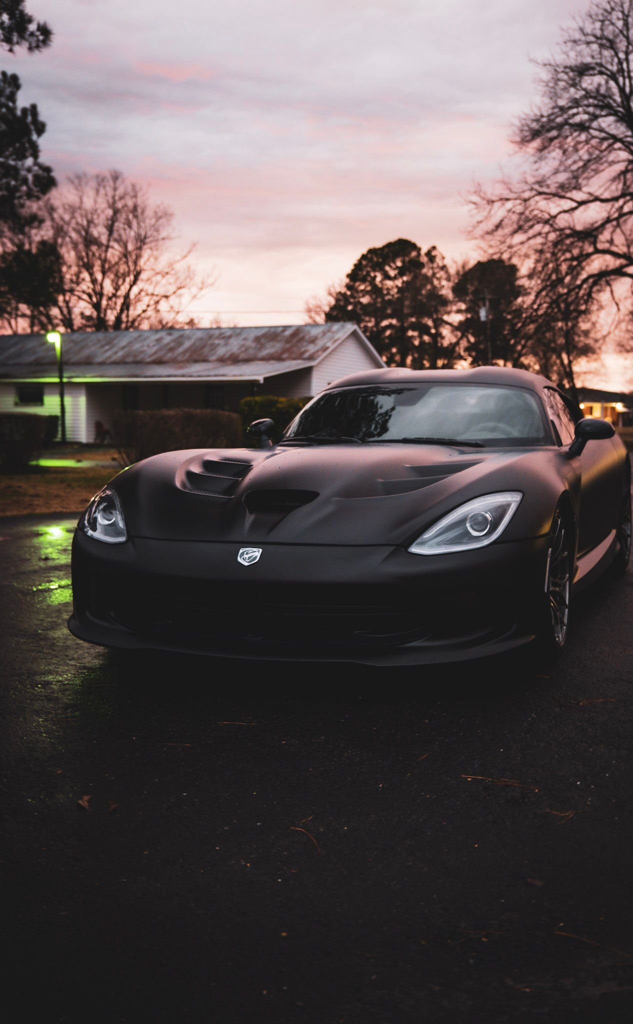 Black Dodge Viper sports car parked on wet asphalt at dusk.