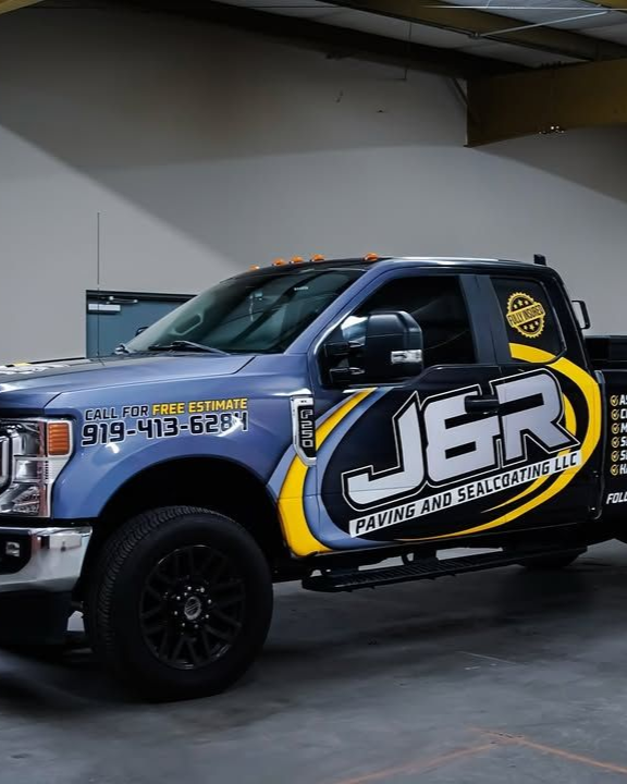 Blue J&R Paving truck with logo wrap, black wheels, phone number on the door, in a garage setting.