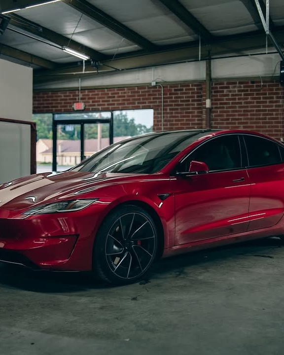 Red Tesla Model S inside a garage with brick walls.