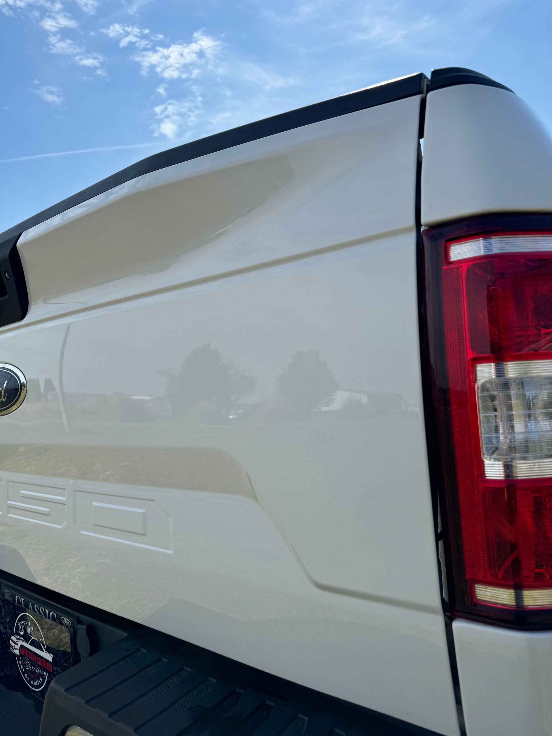 White Ford F-150 truck bed and tail light against a blue sky.