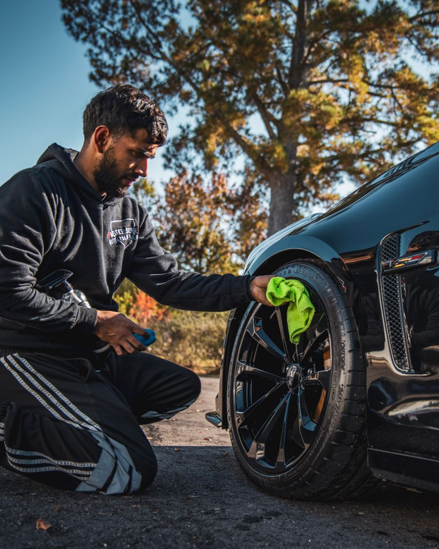 Man cleaning a black car's tire with a green cloth outdoors.
