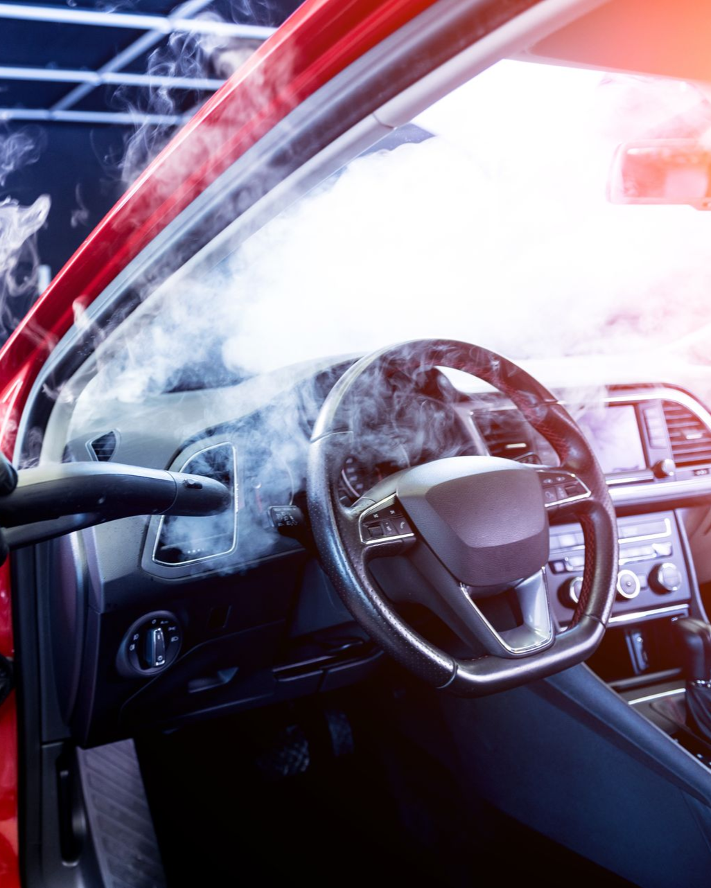 Steam cleaning a red car's dashboard. A steam cleaner nozzle is pointed at the interior.