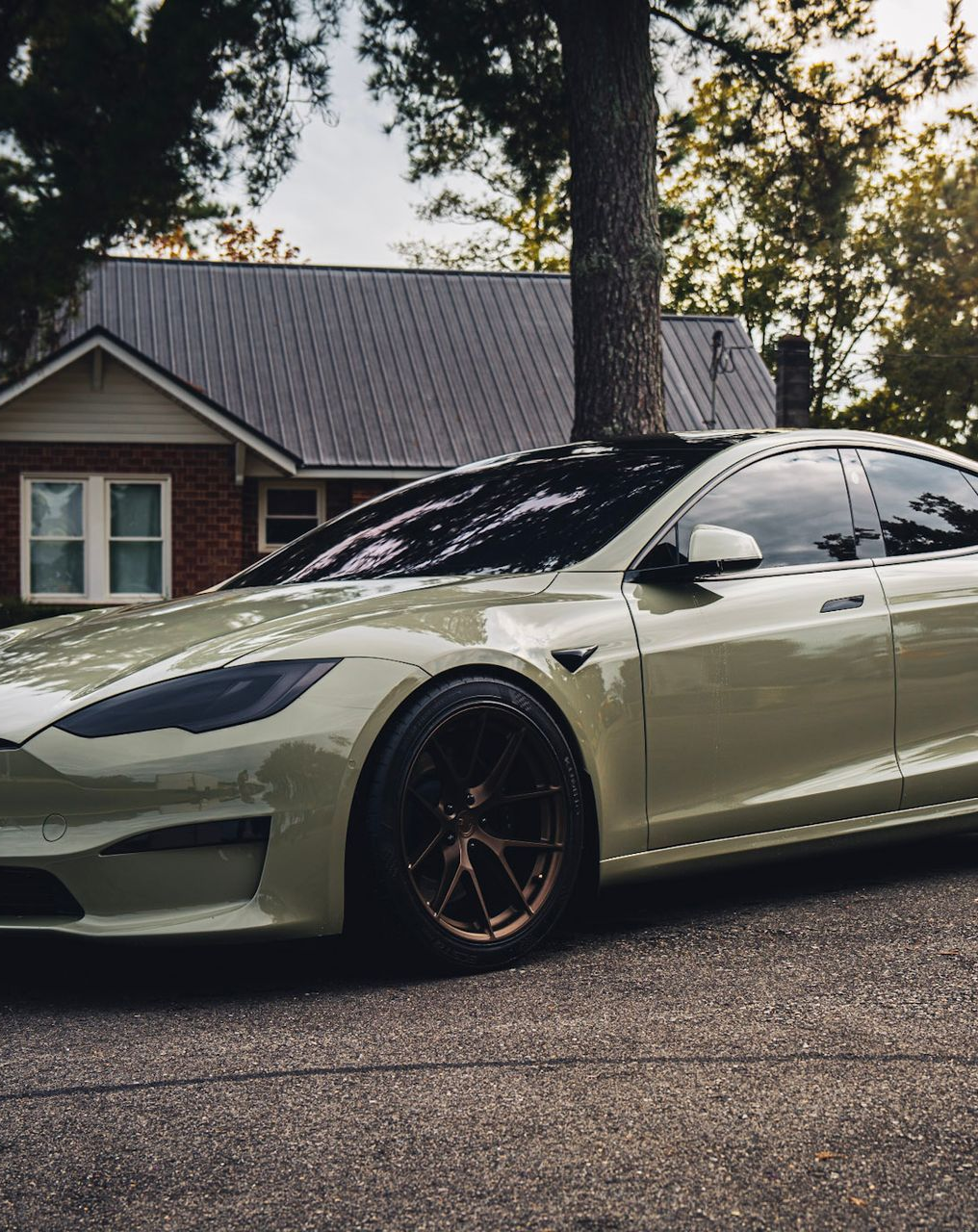 Green Tesla Model S parked on a street in front of a house.