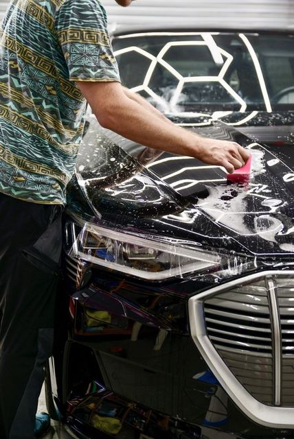 Person washing a black car with a sponge; honeycomb lighting above the car.