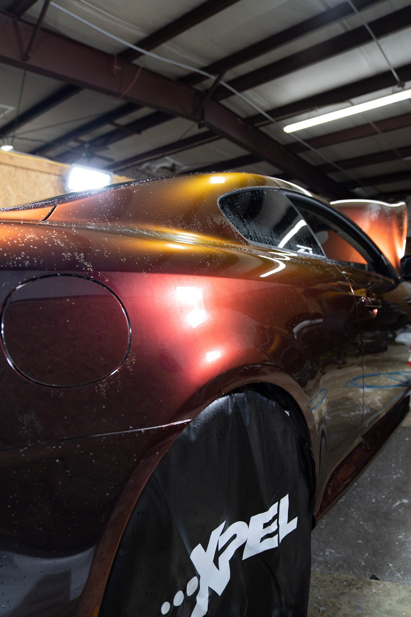 A car with color-shifting paint, inside a garage with bright lights. Protective cover on a wheel.