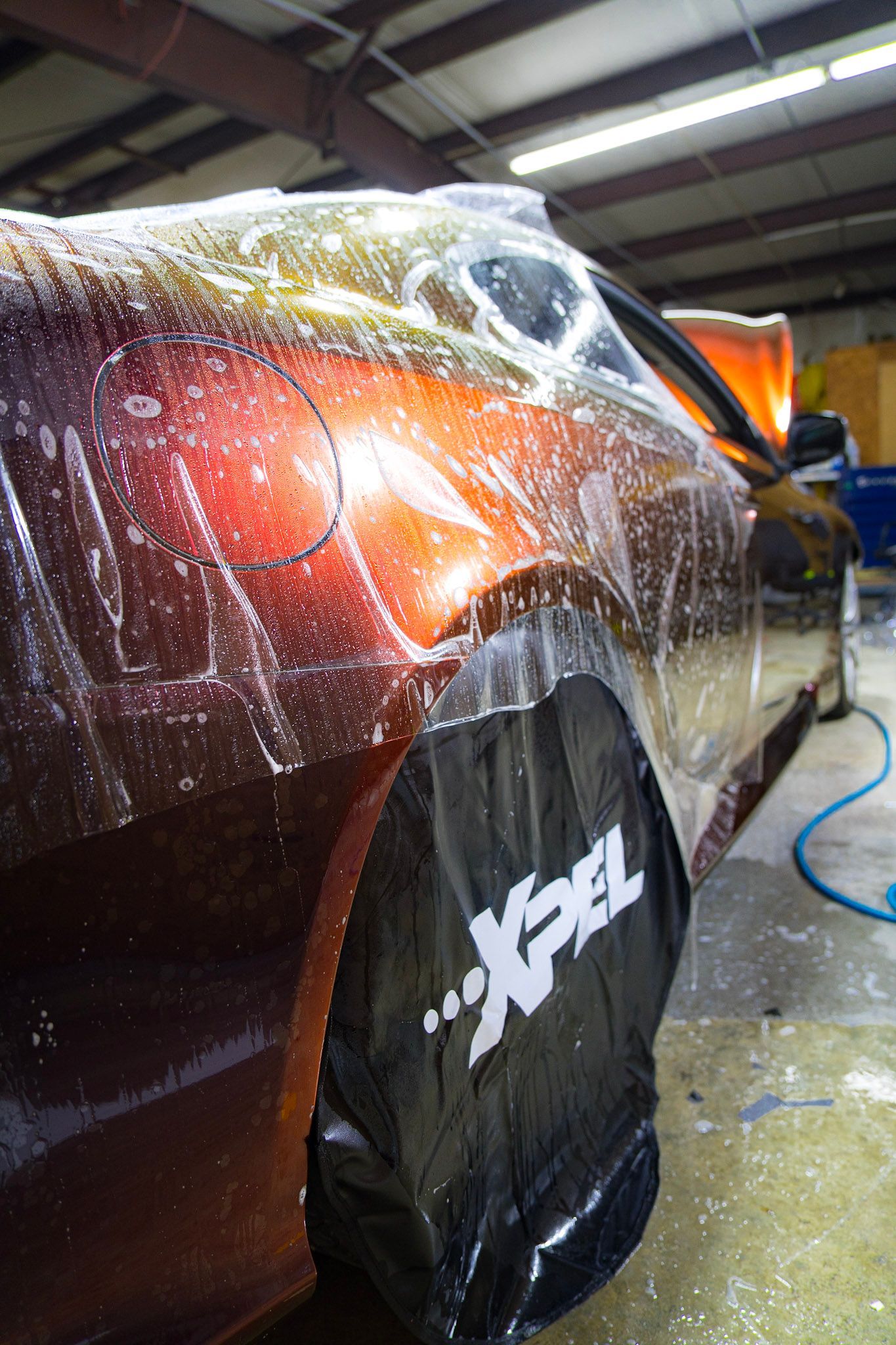 A car with protective film being applied, covered in soapy water, XPEL tire covers.