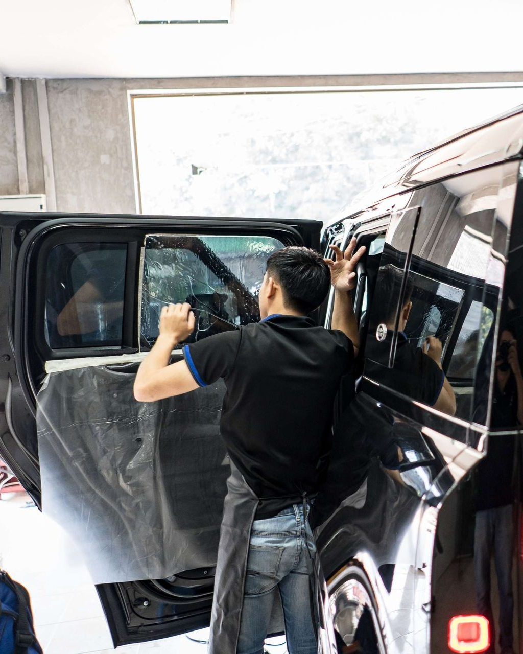 A person applies window tint to a black car door in a shop.