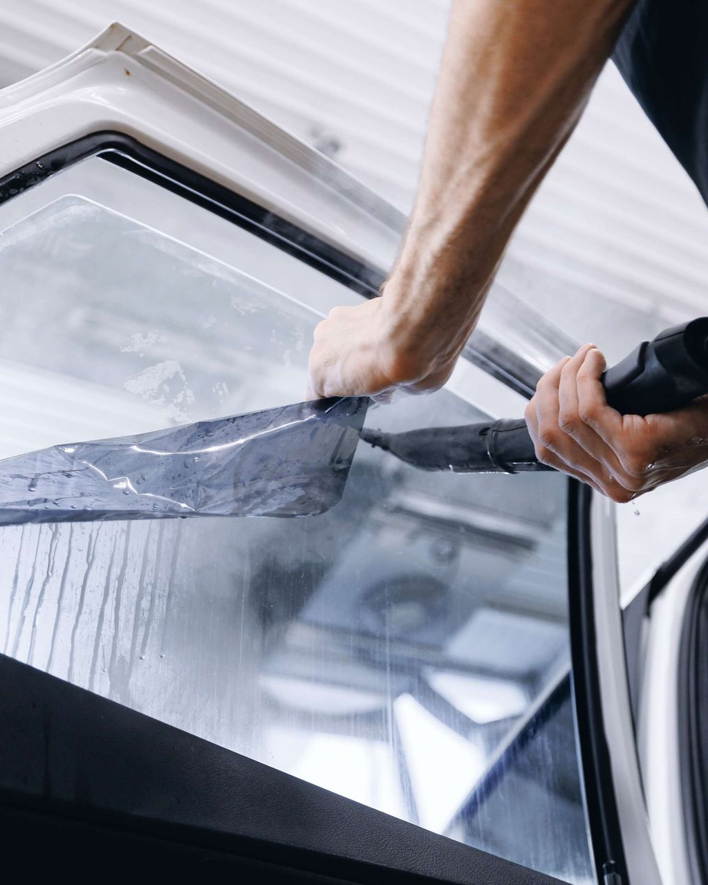 Person applying tinted film to a car window with a squeegee.