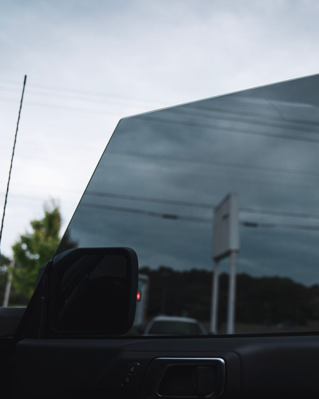 View from a car window with tinted glass. Reflects a cloudy sky and blurred roadside scene.