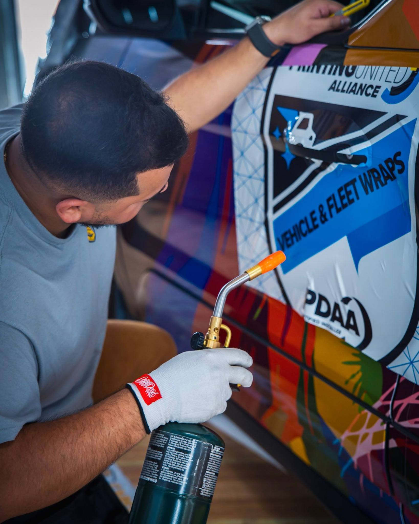 Person using a propane torch on a colorful vehicle wrap, possibly installing it.
