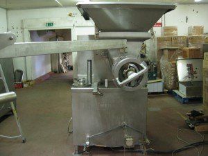 Stainless steel industrial meat grinder in a factory setting.