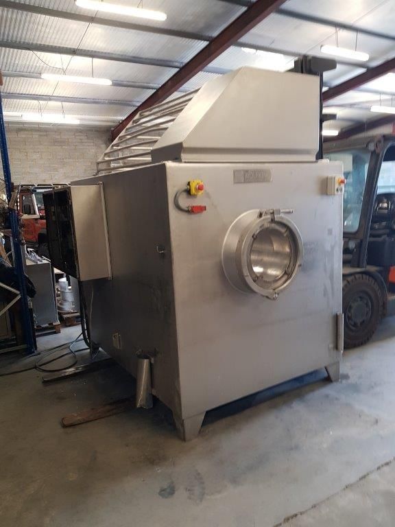 Large stainless steel industrial machine in a warehouse, with a round glass viewing window and control buttons.