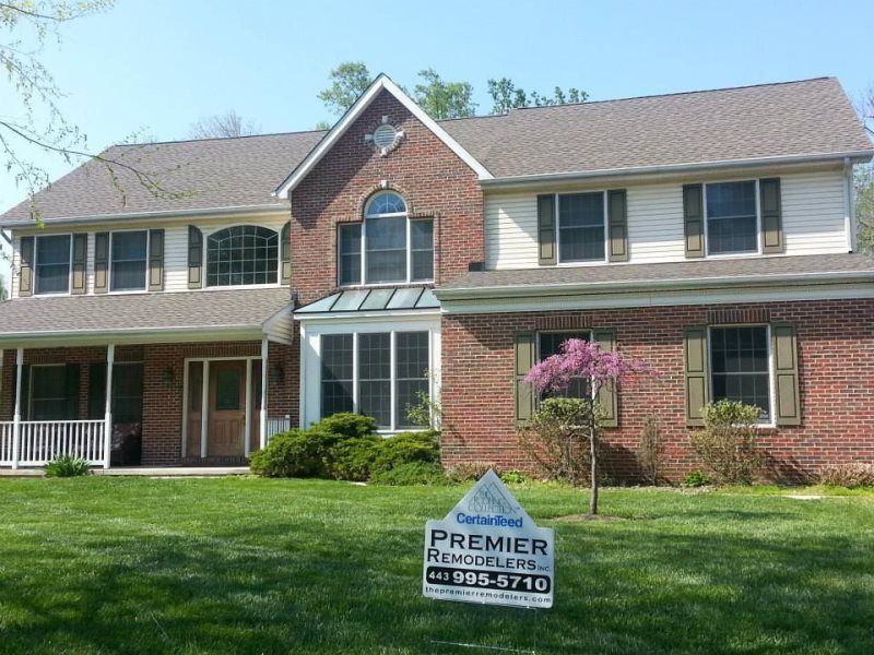 a large brick house with a premier roofing sign in front of it