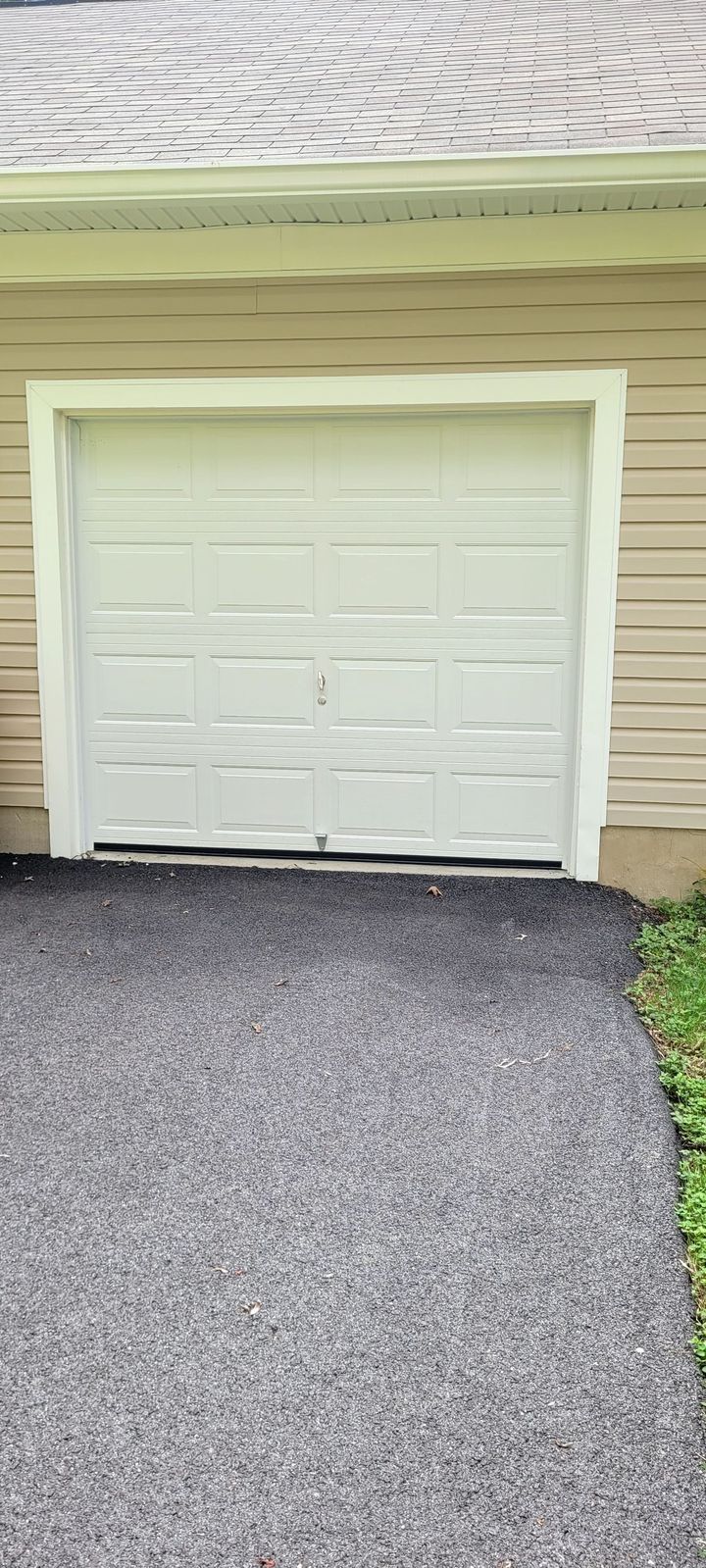 A white garage door is sitting on the side of a house next to a gravel driveway.
