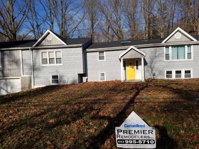 a large gray house with a yellow door and a premier remodelers sign in front of it .