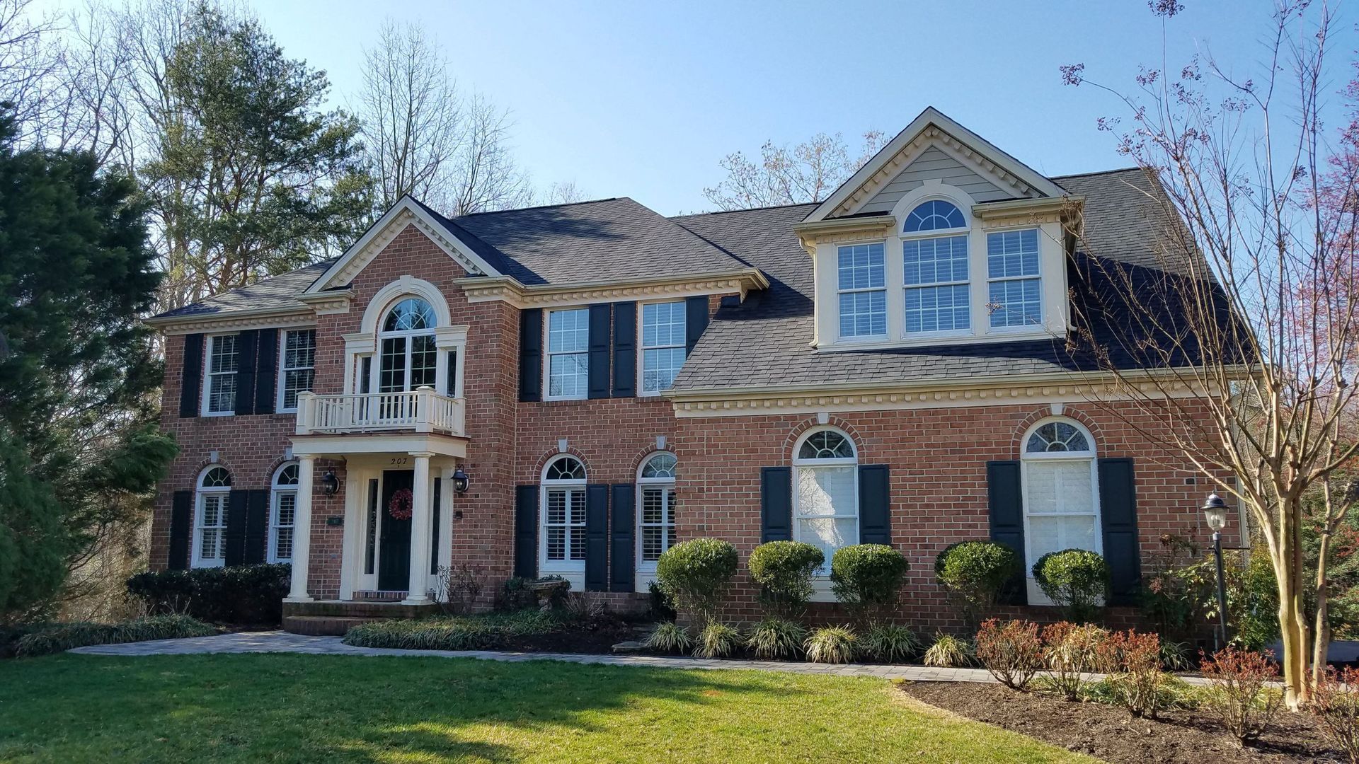 A large brick house with black shutters is sitting on top of a lush green lawn.
