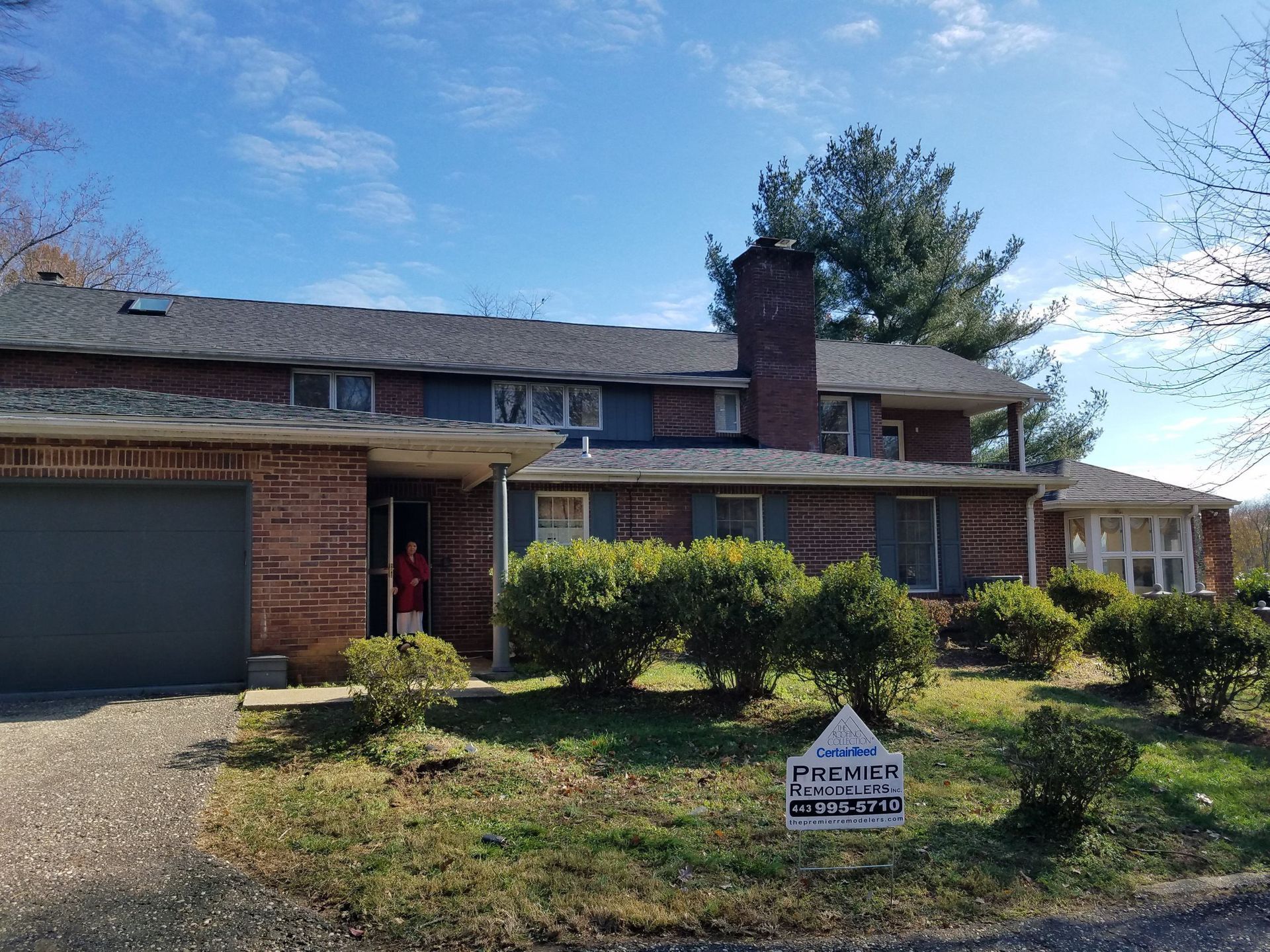 A large brick house with a gray garage door and a for sale sign in front of it.