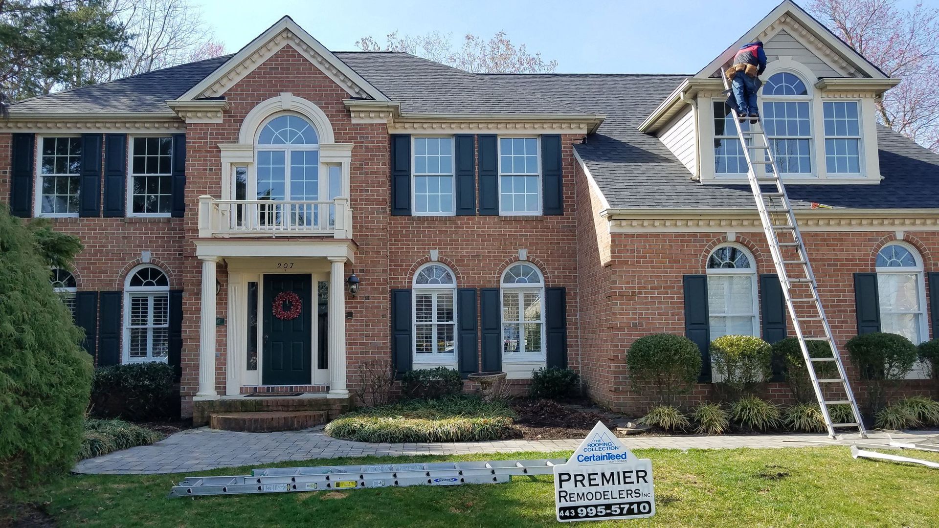 A man is standing on a ladder in front of a large brick house.