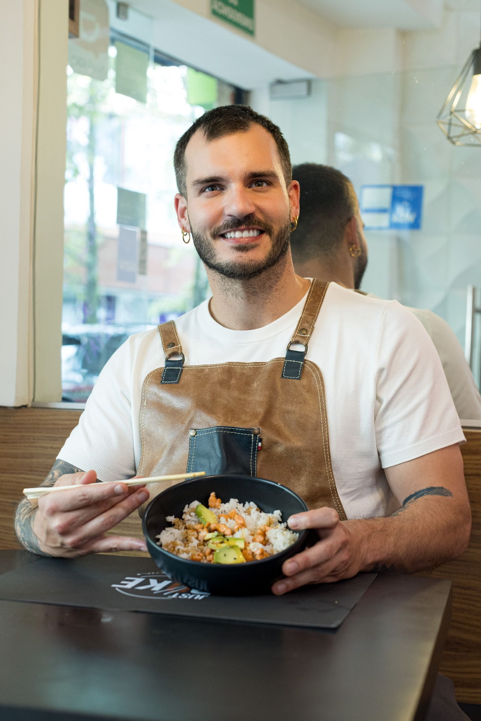 Un hombre que lleva un delantal sonríe mientras sostiene un plato de comida y palillos.