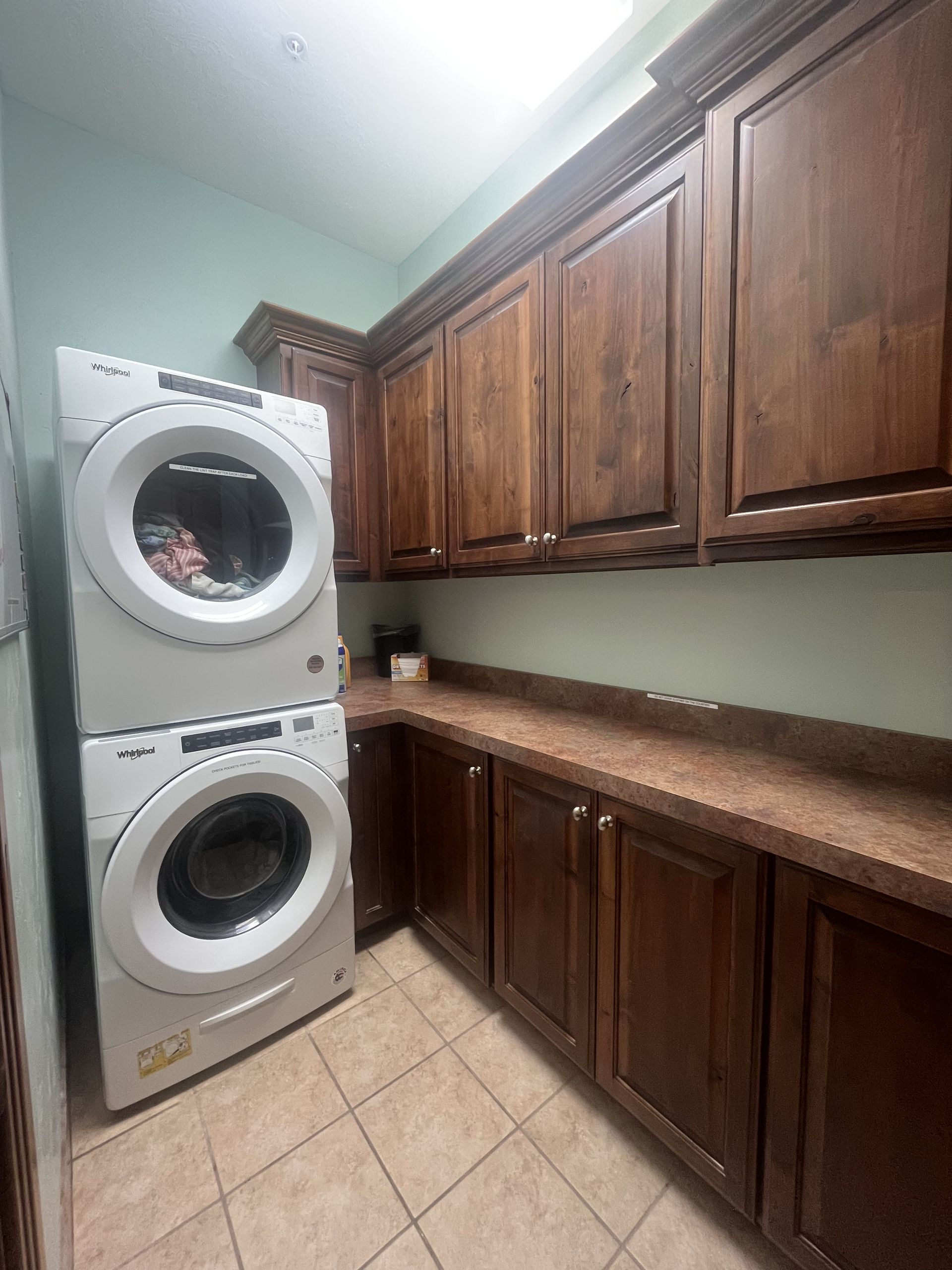 Laundry room with stacked white washer/dryer, brown cabinets, and tan countertop.