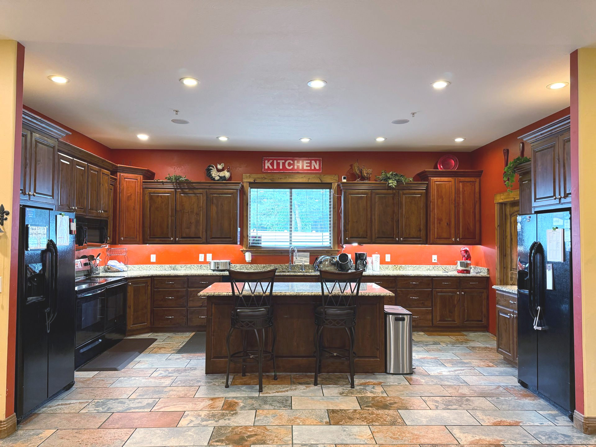 A large, warm kitchen with dark wood cabinets, a center island, and red walls.