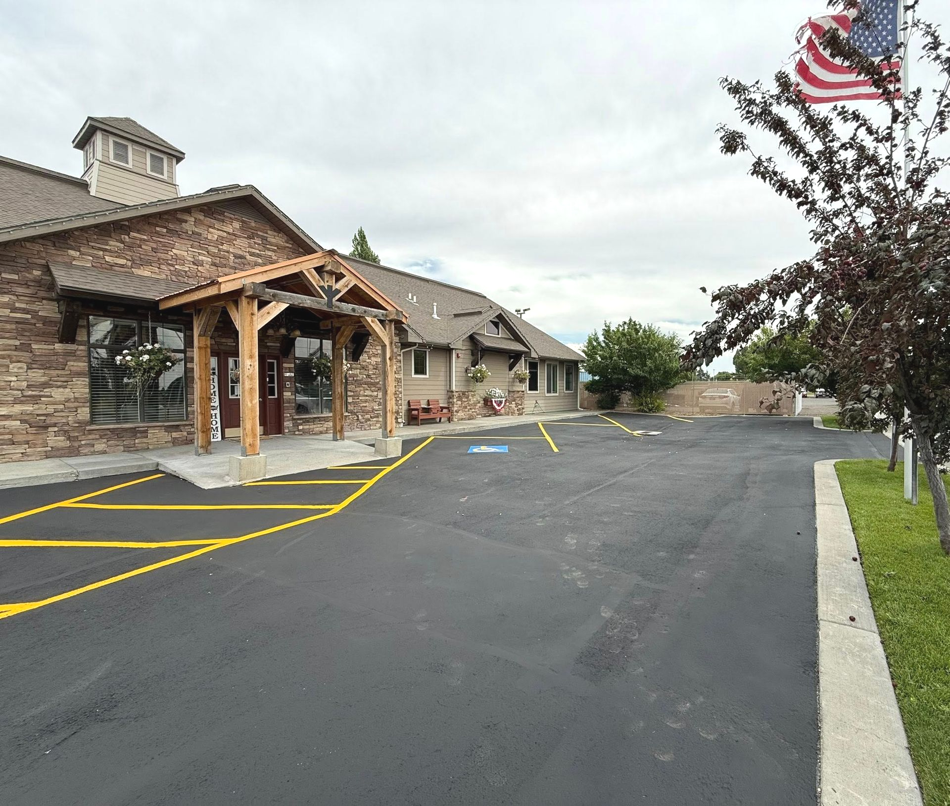 Exterior of a stone building with a wooden awning, a parking lot, and an American flag.