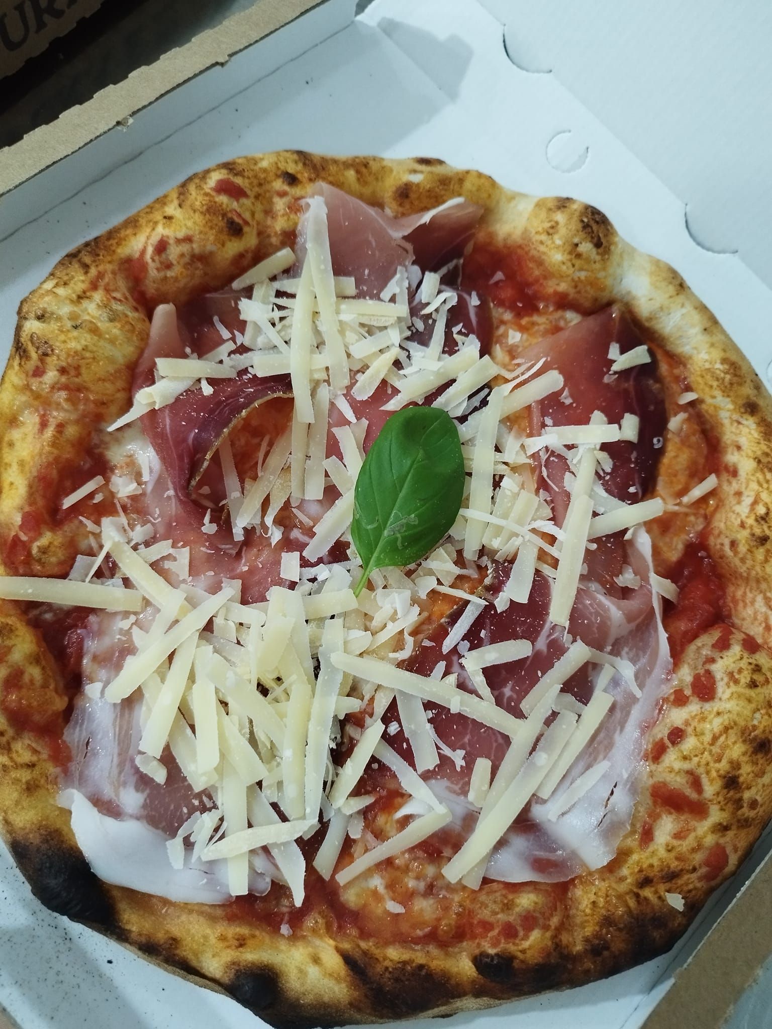 Una pizza con prosciutto e formaggio è in una scatola