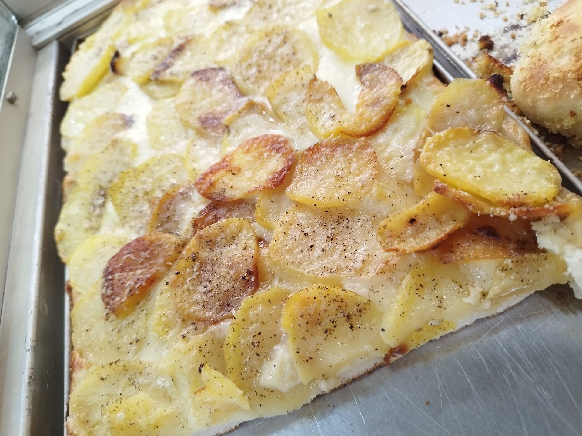 Una fetta di pizza con sopra delle patate è su un vassoio.