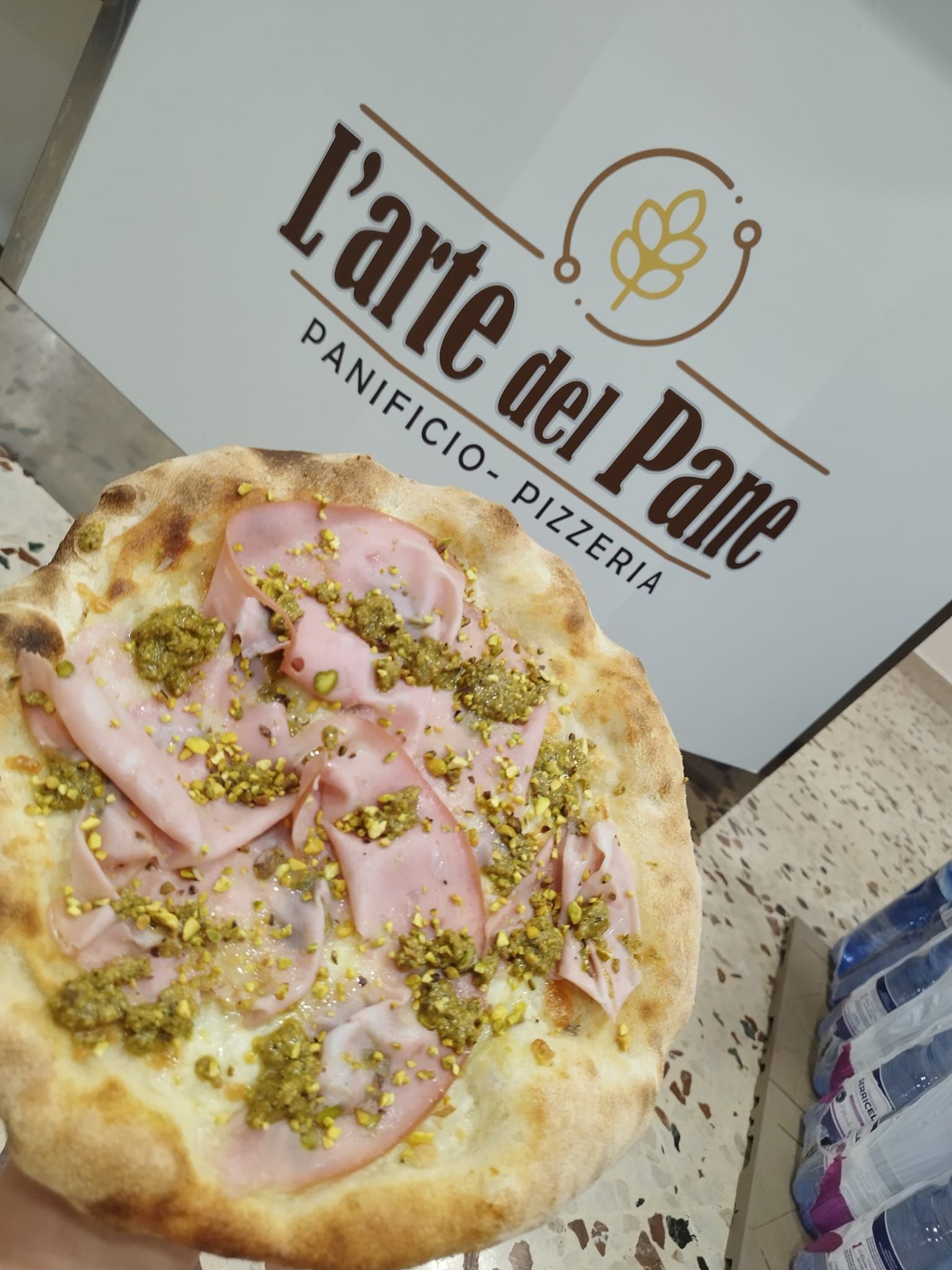 Una persona tiene in mano una pizza davanti a un cartello che dice l'arte del pane