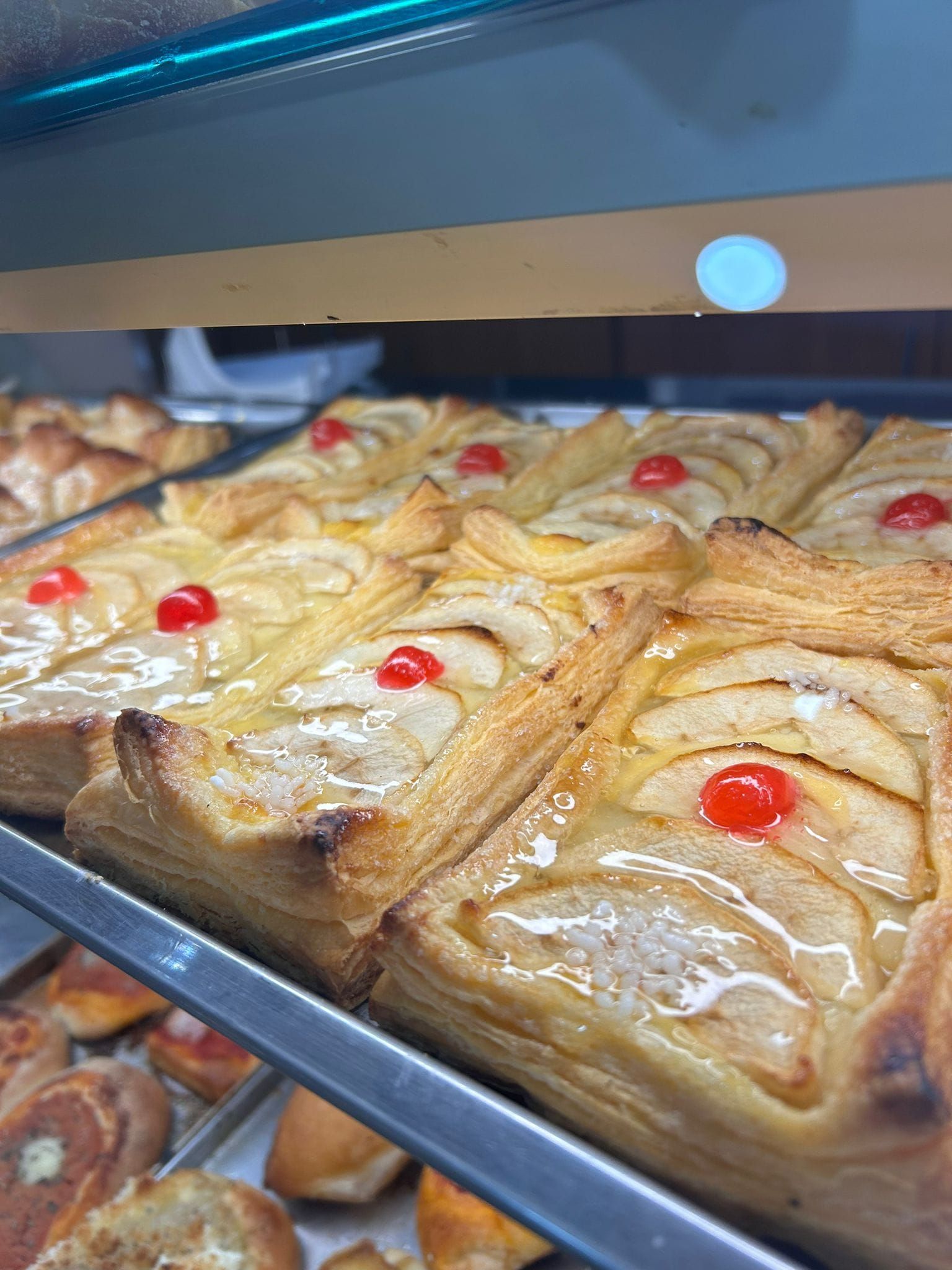 Un mucchio di pasticcini alle mele con ciliegie sopra sono appoggiati su uno scaffale.