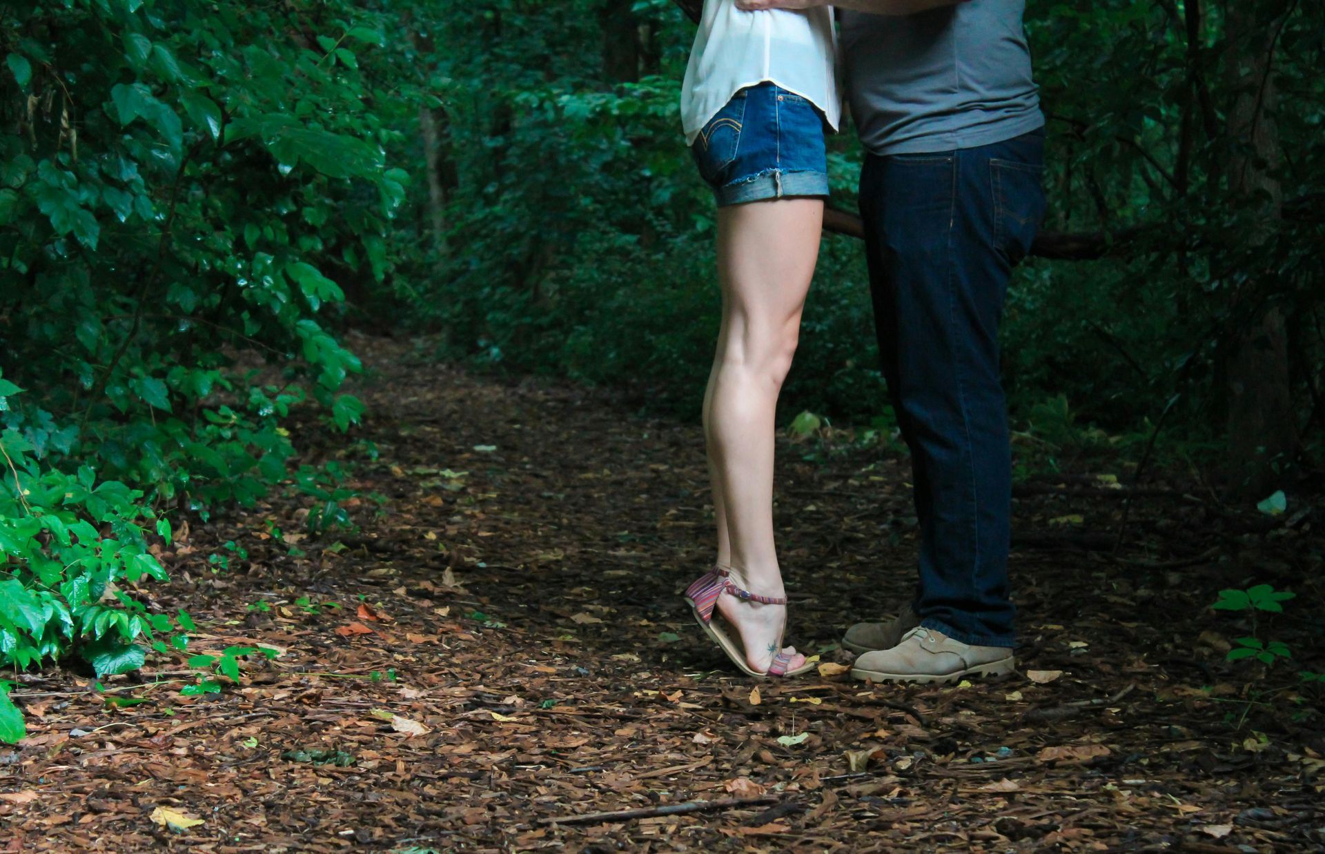 A man and a woman are kissing on a path in the woods.