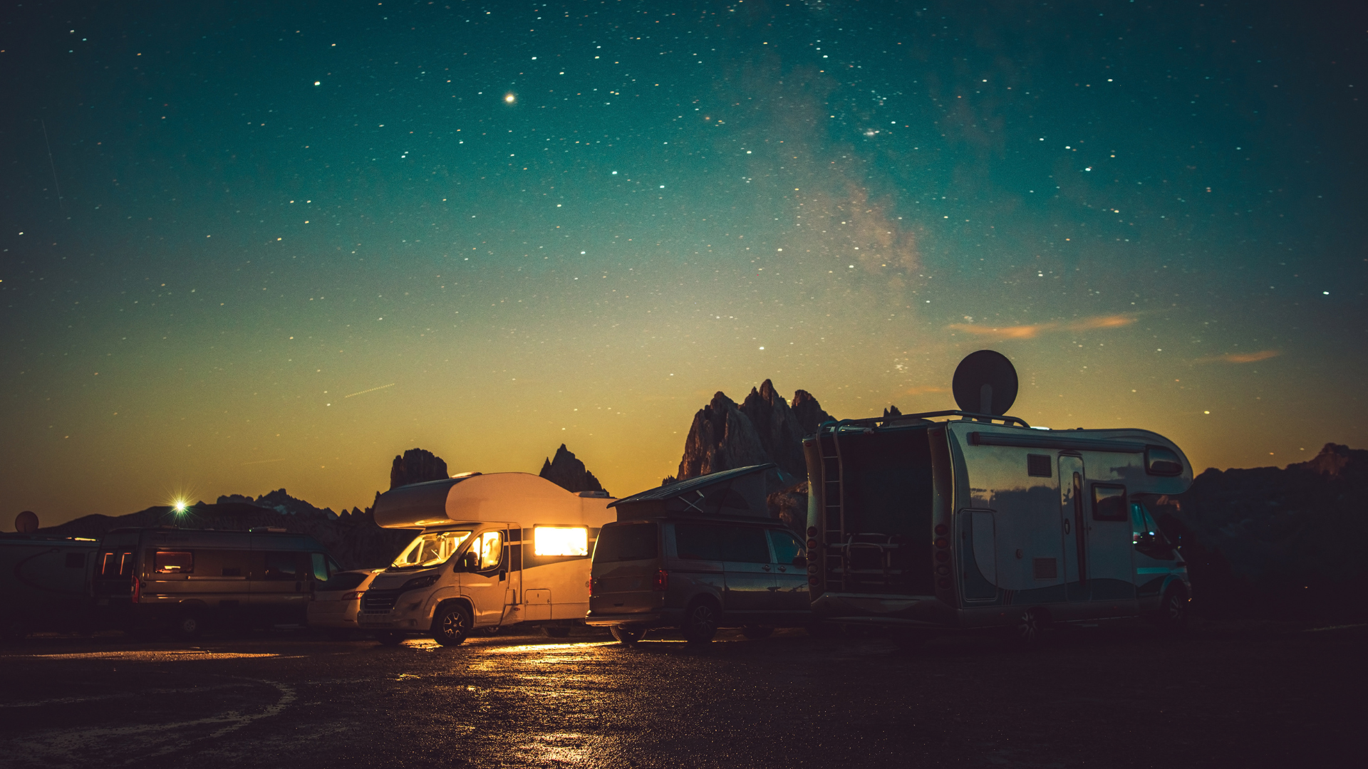 Campers under a starry night sky. Illuminated RVs parked with a mountain silhouette.