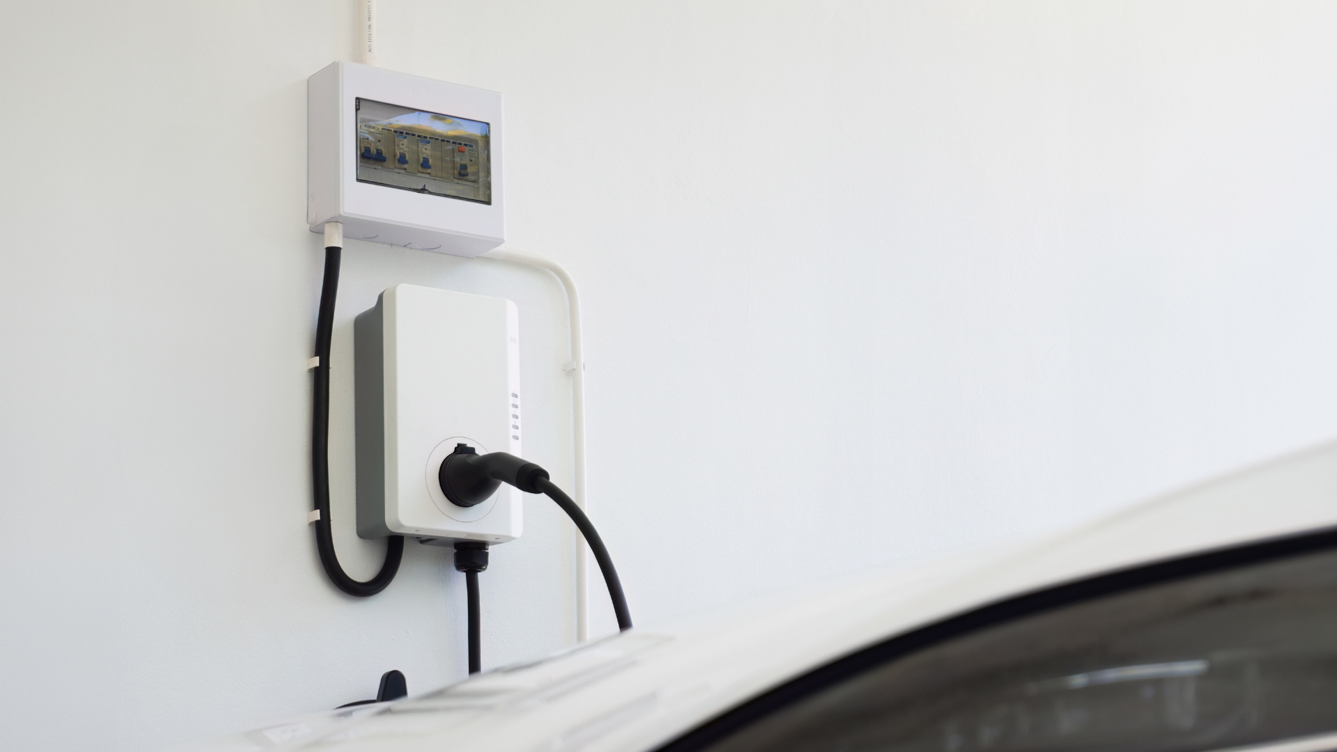 Electric vehicle charger mounted on a white wall, charging a car; black cable plugged in.