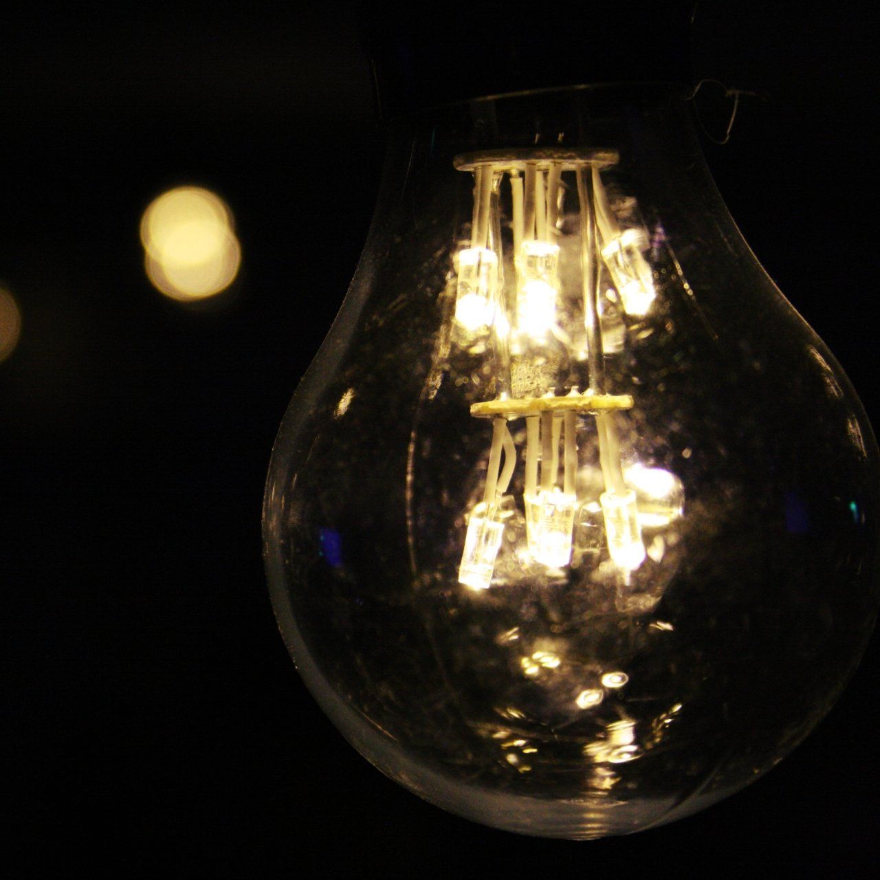 Close-up of a glowing lightbulb in a dark setting, showcasing internal filaments with a blurred background.