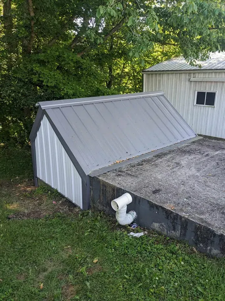 A shed with a metal roof is sitting in the grass next to a house.