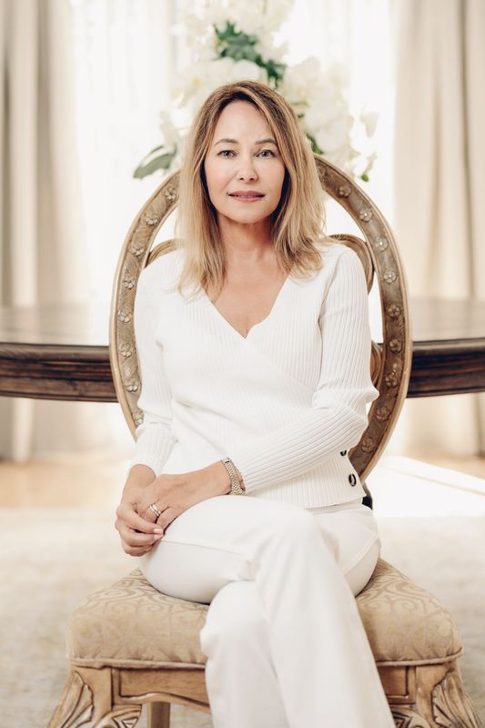 Woman in white outfit sitting in ornate chair. Large flower arrangement in the background.