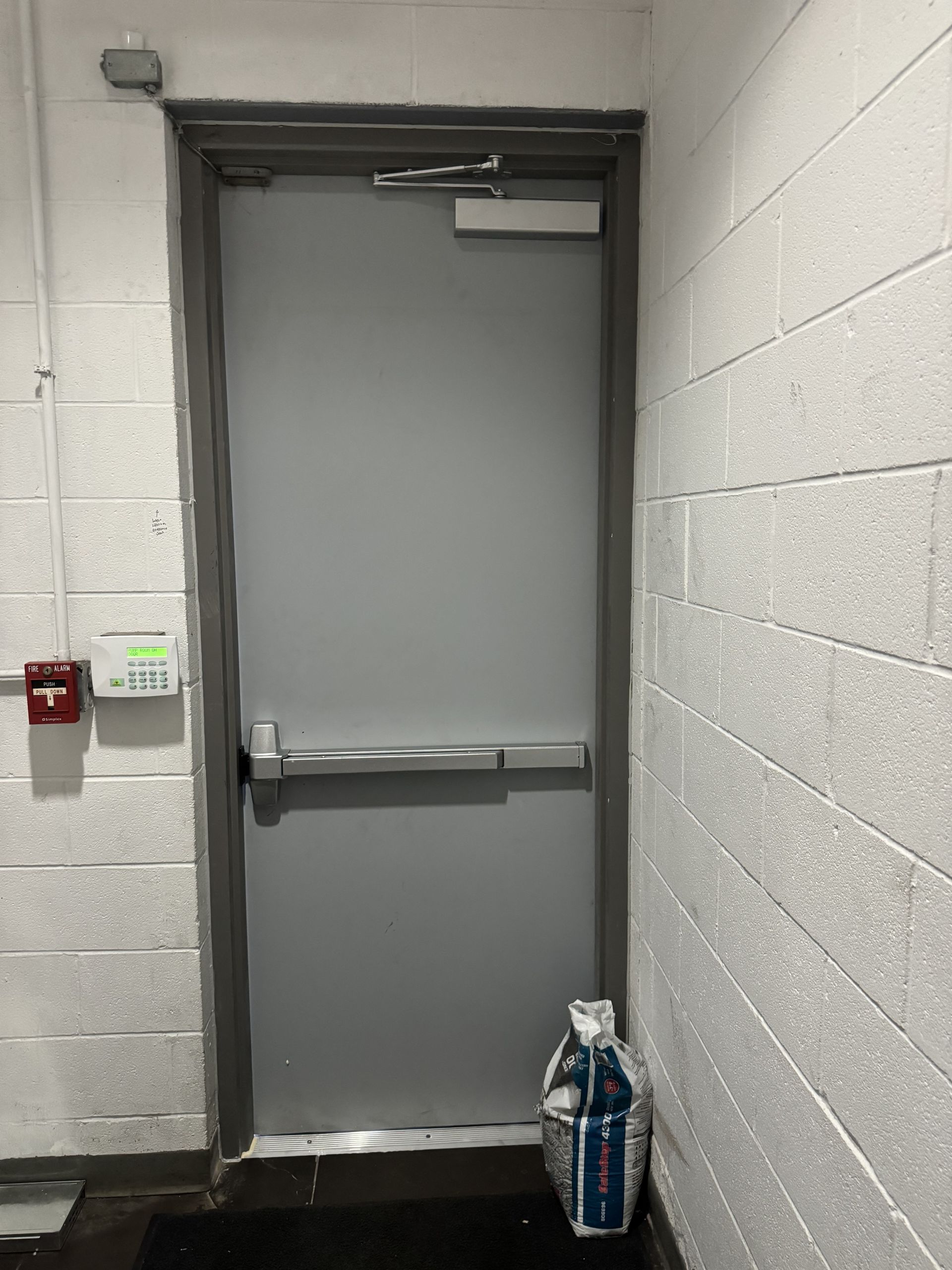 A gray door is sitting in a hallway next to a brick wall.