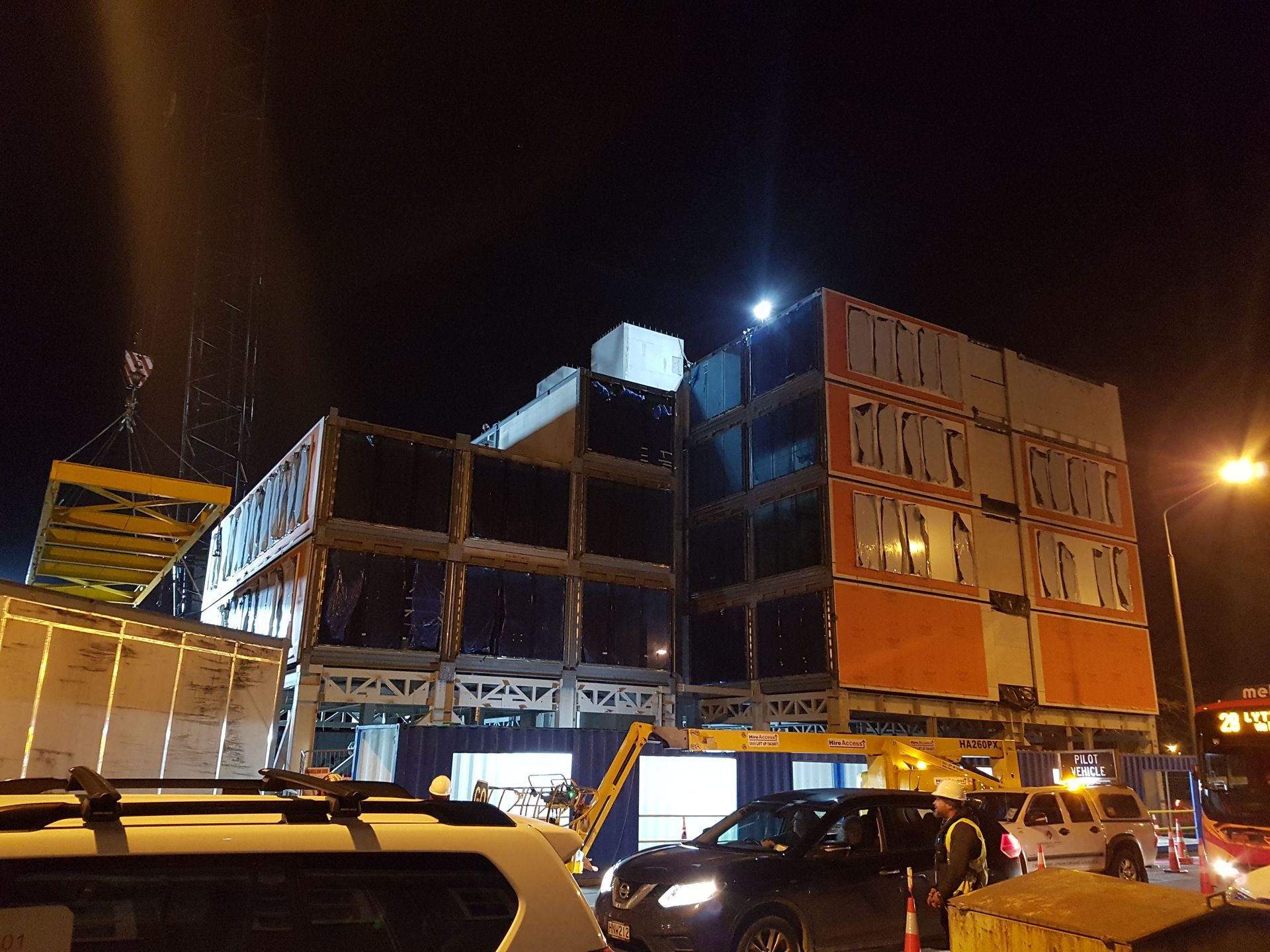 A large building is being built at night with cars parked in front of it