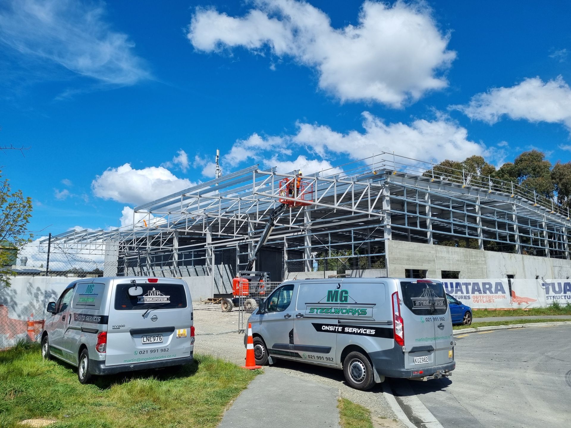 Two vans are parked in front of a building under construction.