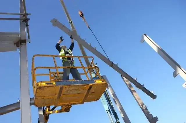 A construction worker is standing in a bucket on a lift
