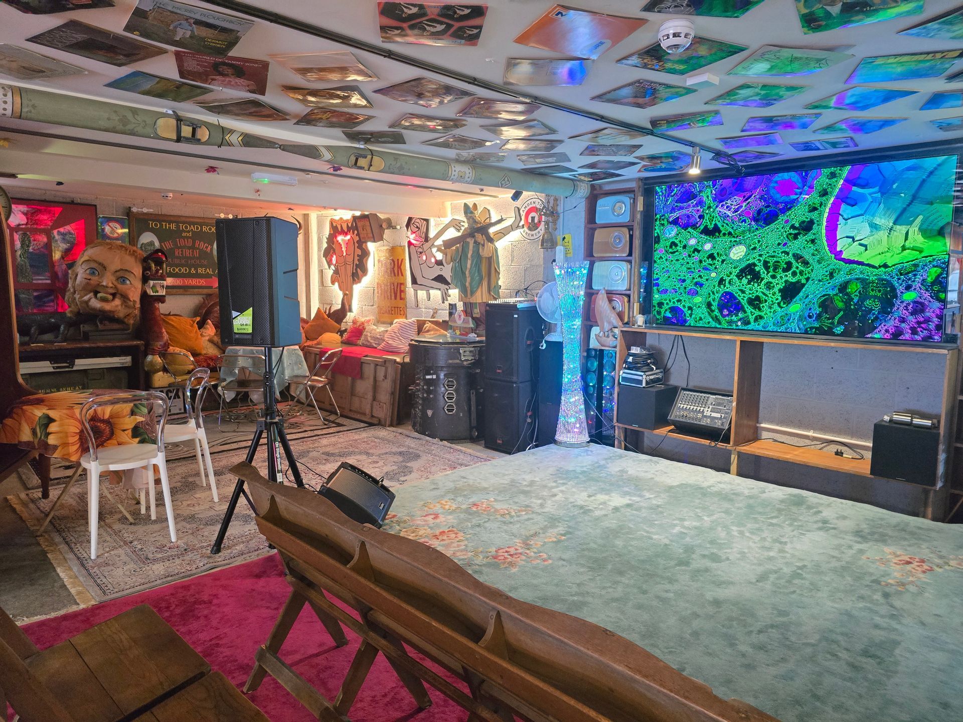 Cozy living room with a couch, tripod, colorful wall art, and a large TV displaying bright abstract patterns.