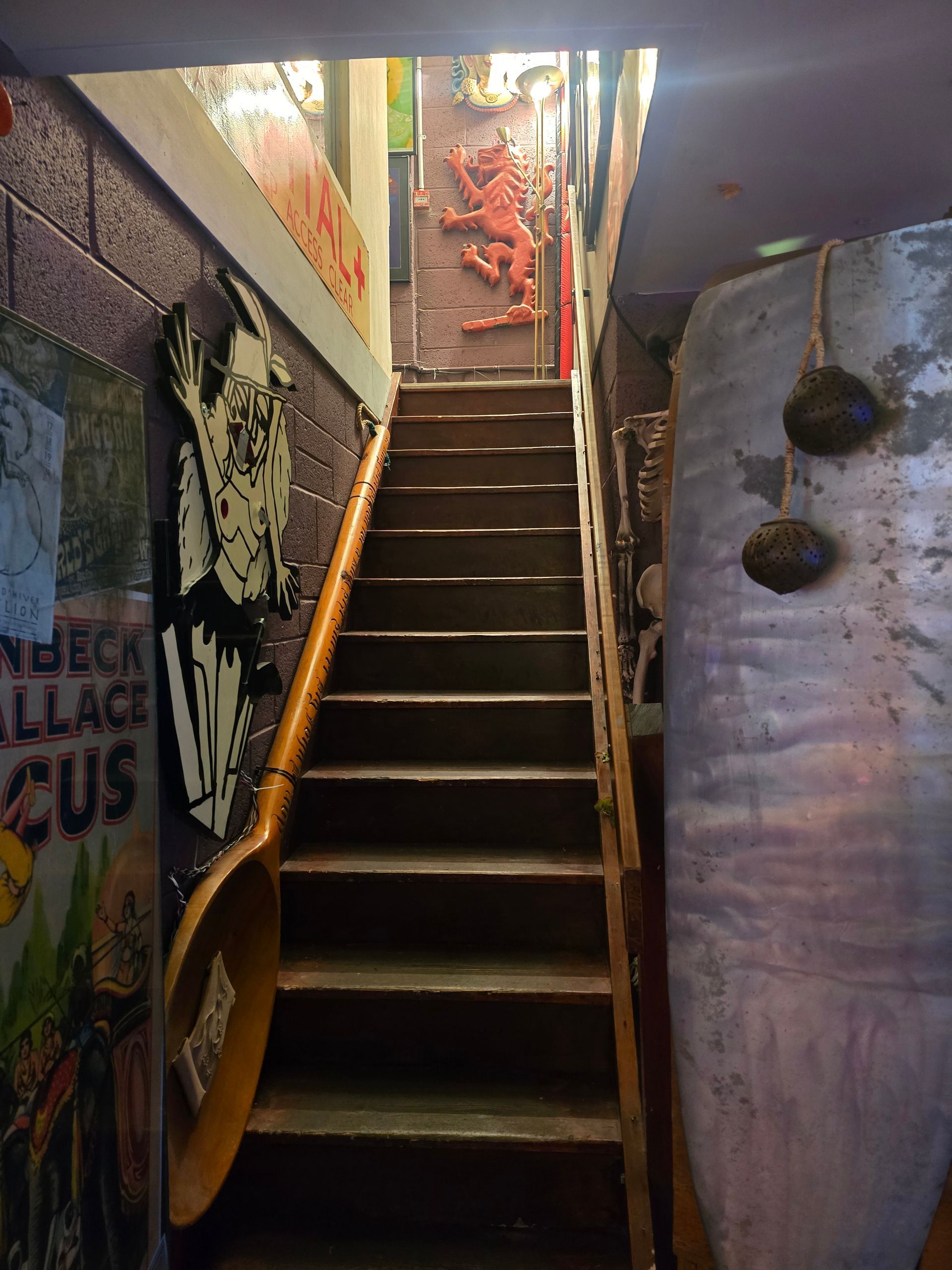 Narrow stairway in a dim indoor corridor, with colorful wall art and hanging pots beside the steps