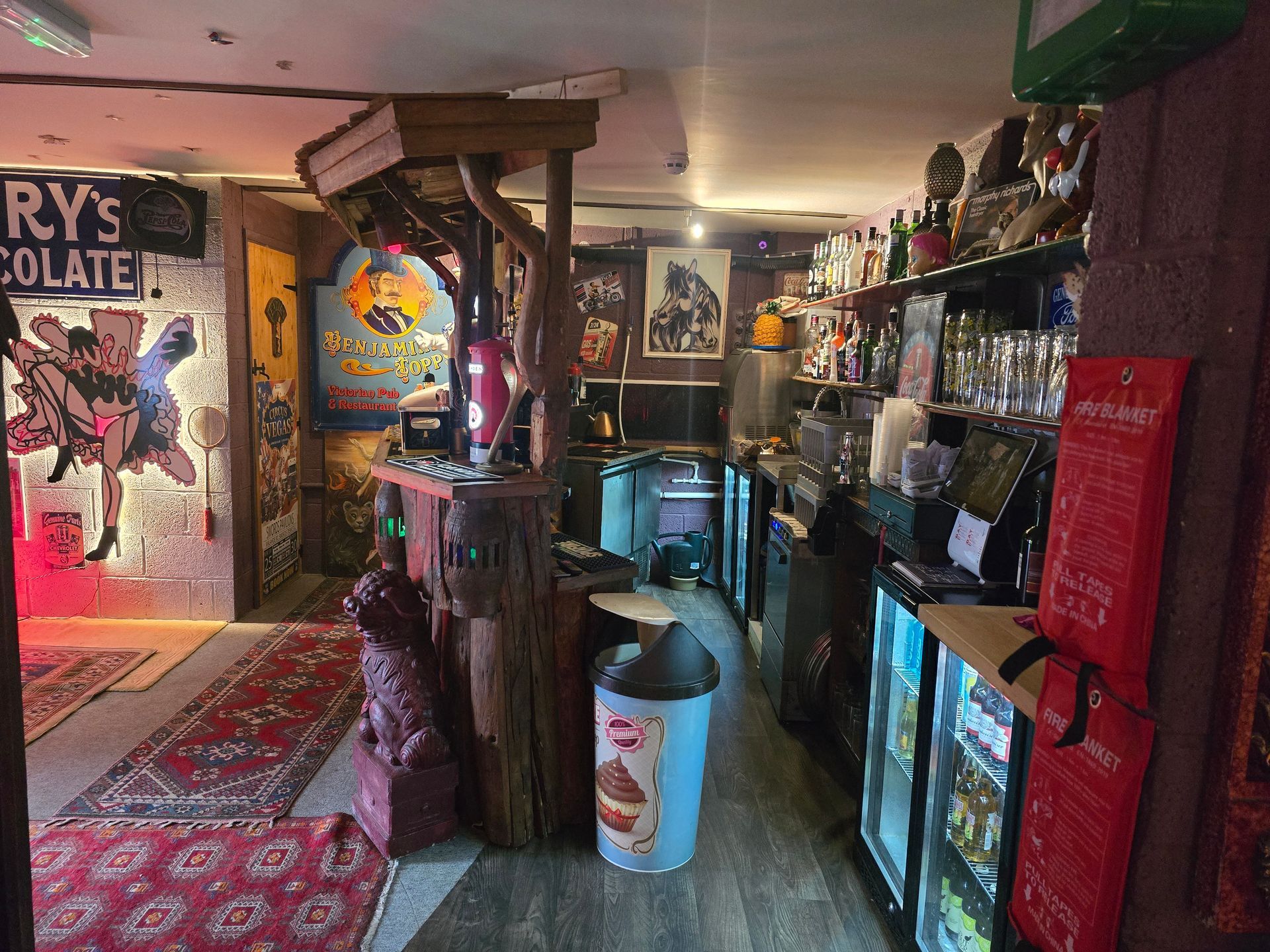 Cozy bar interior with colorful decor, wooden posts, and a lit glass display counter.