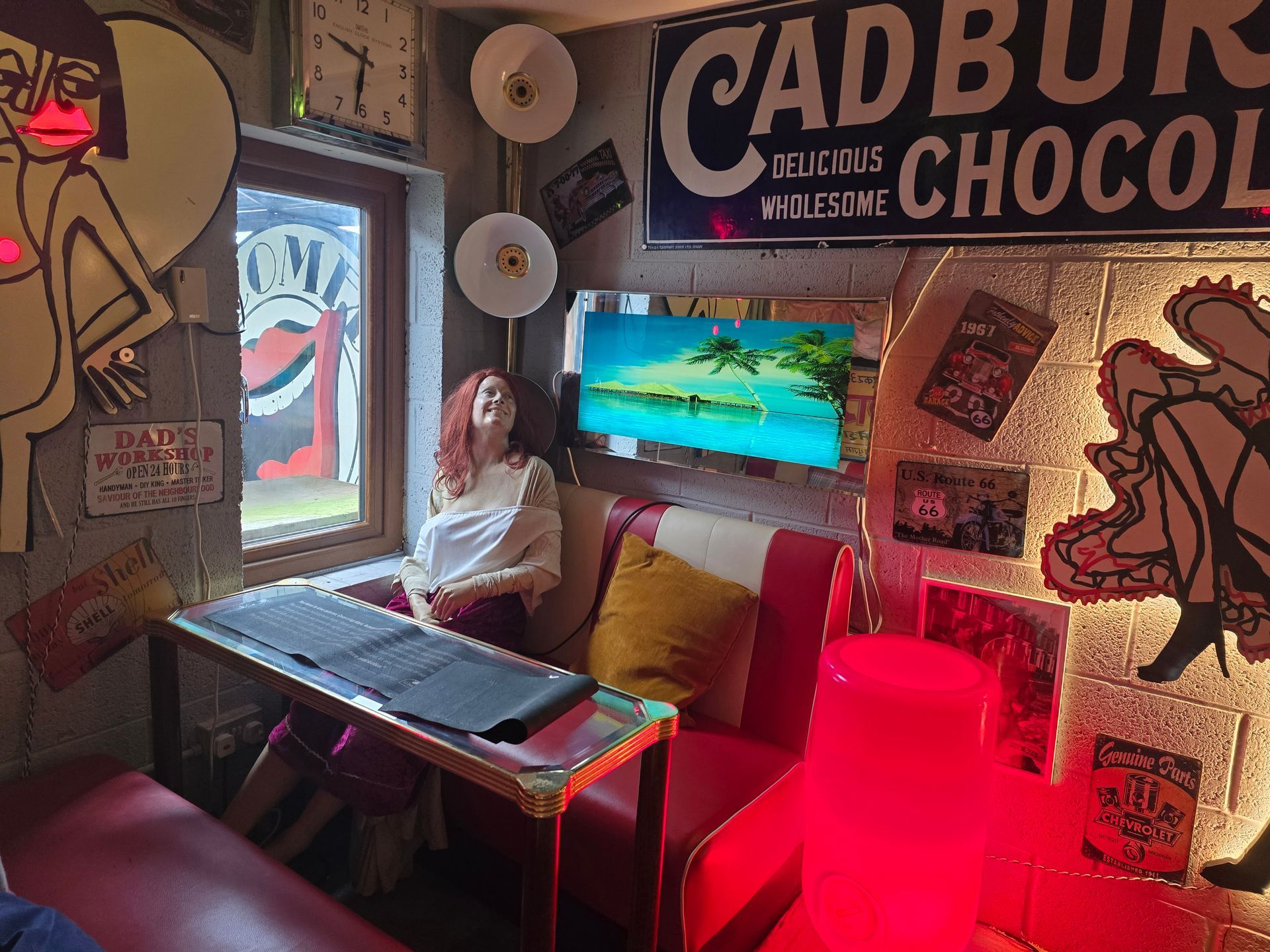 Person sitting in a cozy Cadbury chocolate-themed room beside a small table and bright red lamp