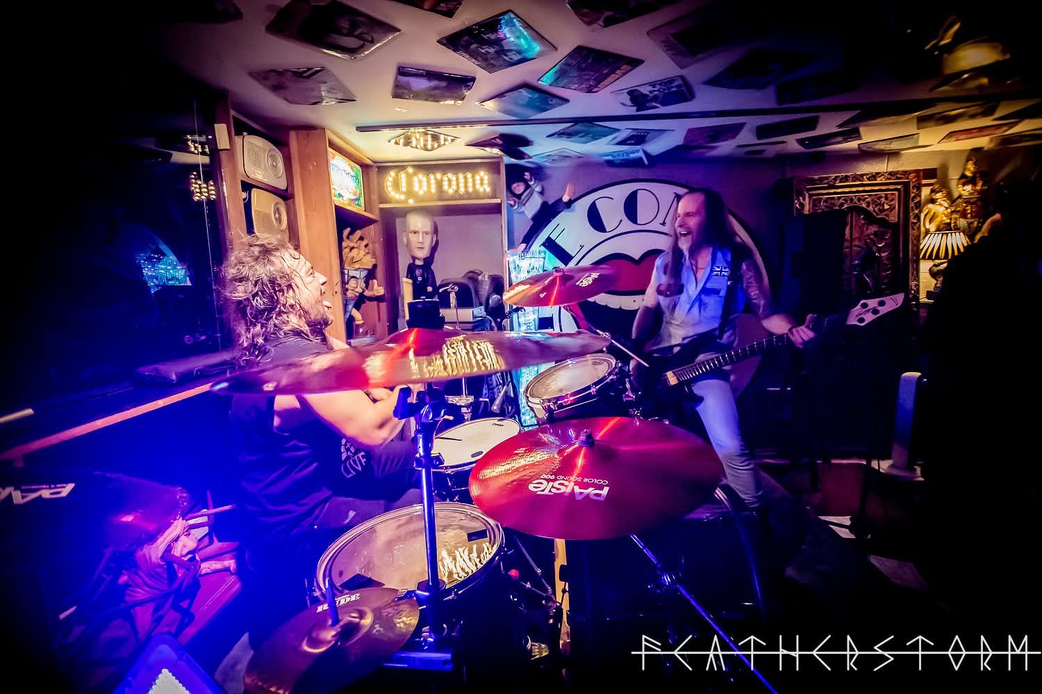 Dimly lit live music venue with a drummer onstage under purple and blue lights