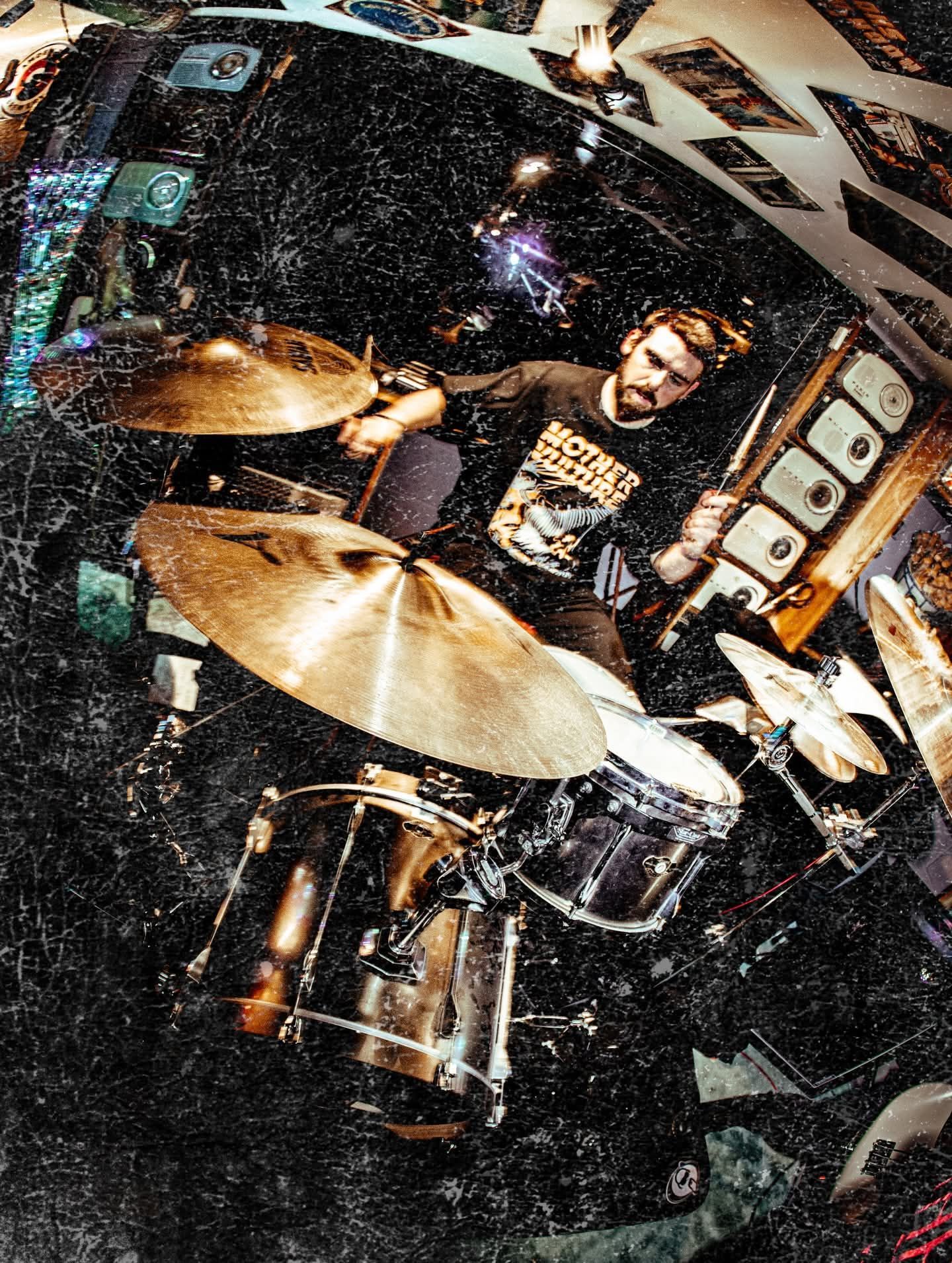 Drummer playing a kit in a dark studio, with cymbals in the foreground and a dynamic, grainy look