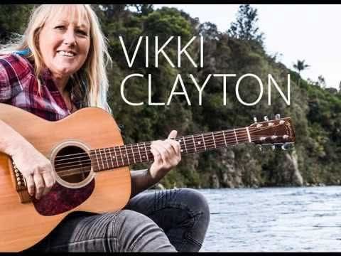 Woman playing acoustic guitar by water with “VIKKI CLAYTON” text overlay