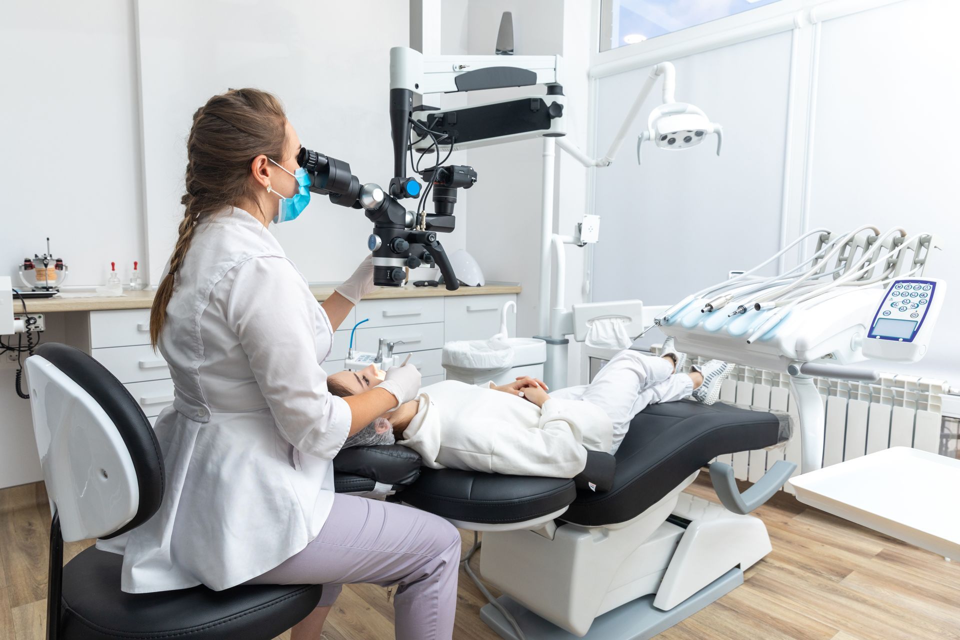 A dentist using a dental microscope and treating a patient at a dental clinic.