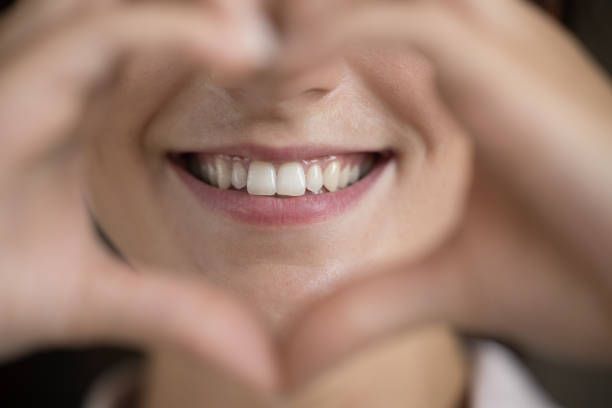 A young woman making a heart sign, showing straight white teeth, thanks to expert dental services